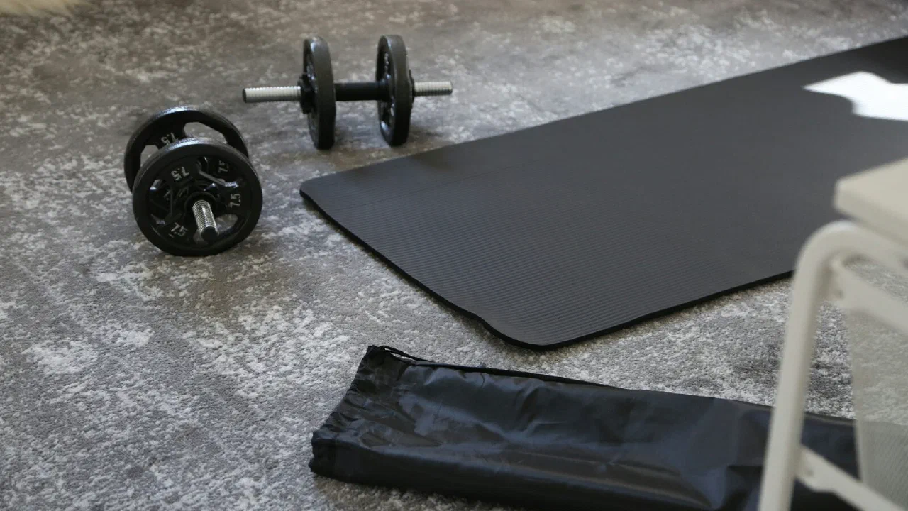 A pair of small dumbbells beside a rolled black mat on a studio floor