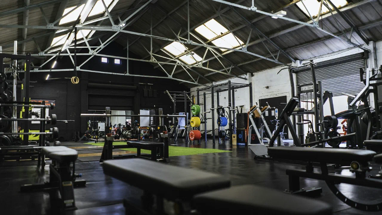 Rows of weight benches and racks in an empty industrial gym with a high ceiling